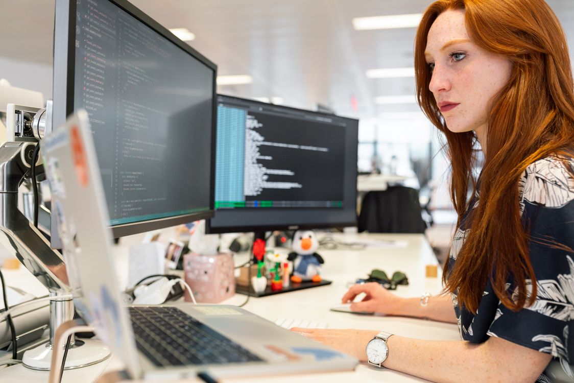 Female software engineer focused on coding across dual monitors in a modern office